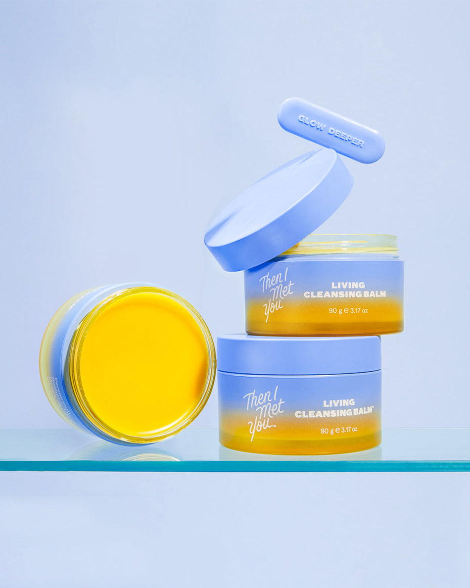 Two stacked jars and one open jar of yellow lip balm with light blue lids on a reflective surface against a light blue.
