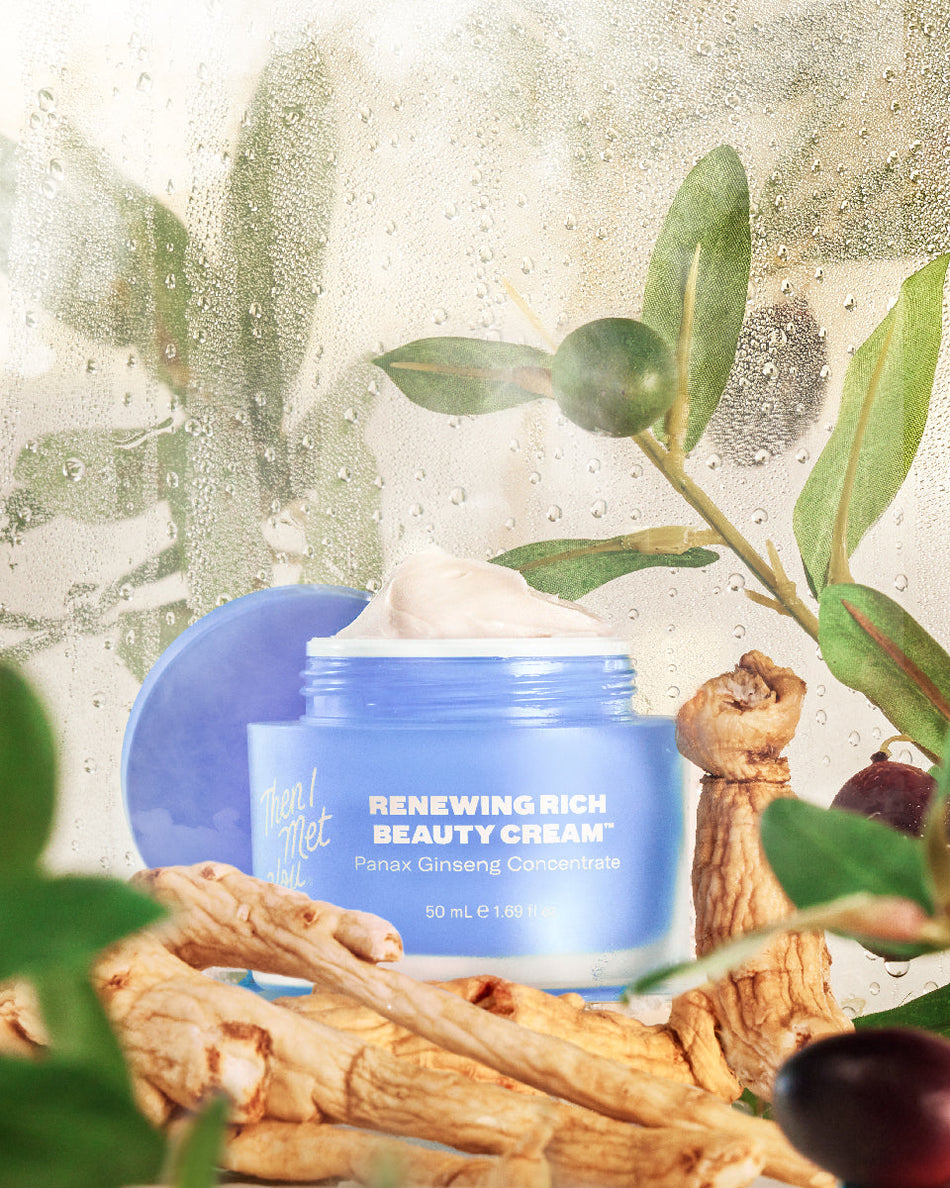 Open blue jar of Renewing Rich Beauty Cream with cream swirl inside on natural wood pieces and green leaves background.